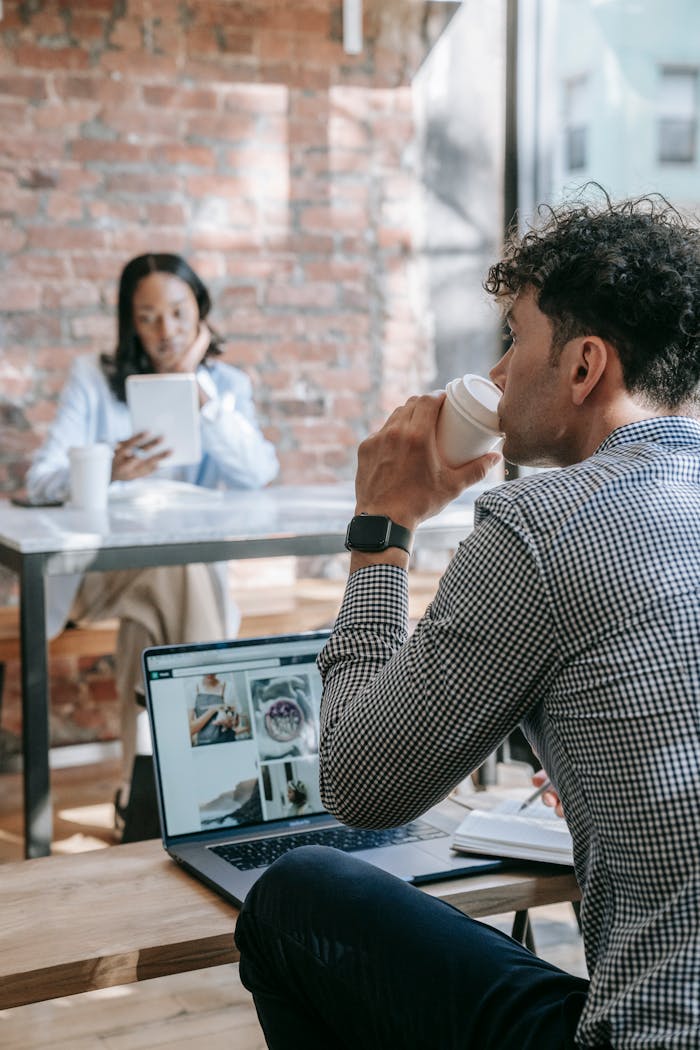 Two adults in a stylish coffee shop setting with laptops and coffee cups, creating a calm and productive workspace.