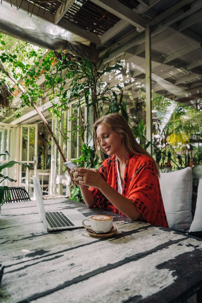 Adult woman in a cafe working remotely on a laptop with coffee and phone.